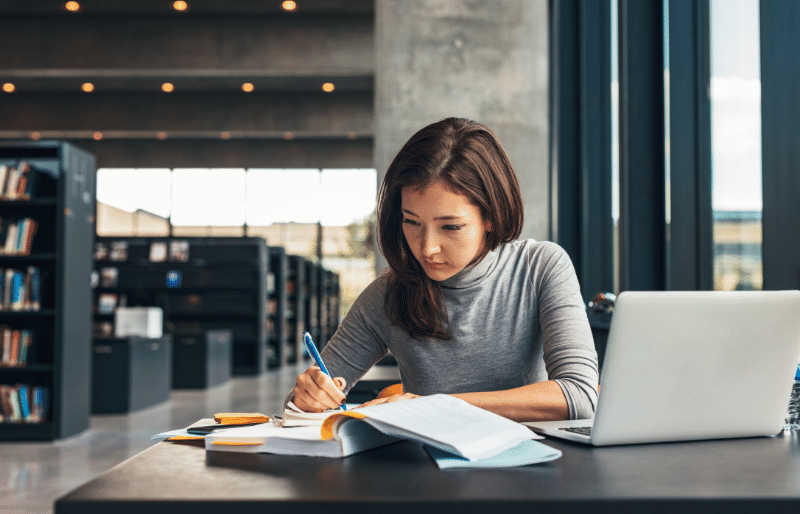 A student studying with a laptop and a stack of books, representing the need for federal student loans